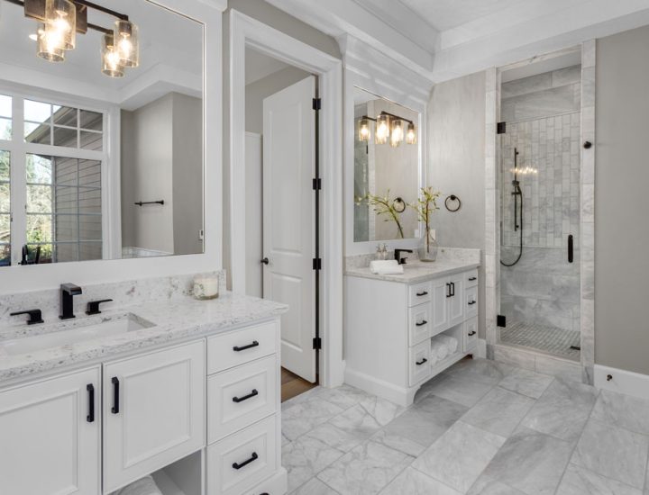 A luxurious bathroom with marble flooring and countertop, mirrors, and mounted light fixtures mounted on it.